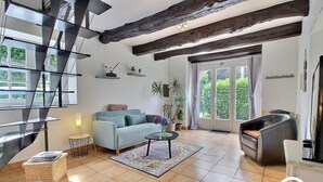 Una sala de estar moderna con sofá, una mesa de centro y chimenea. Se observa una escalera con barandillas de vidrio y vistas a áreas verdes.