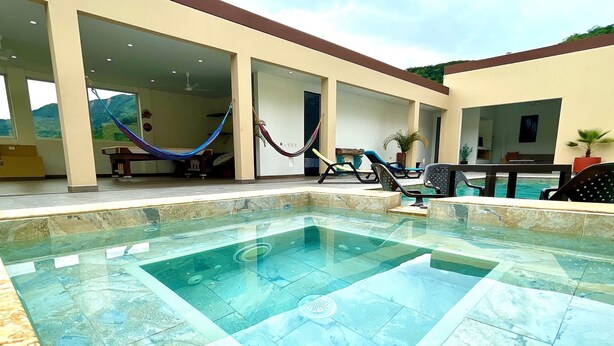 Une piscine avec une terrasse carrelée, un hamac et des chaises longues.