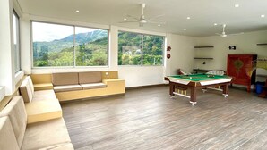 Une pièce équipée d’une table de billard, d’un canapé et de grandes fenêtres donnant sur les montagnes.