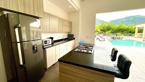 Une cuisine moderne équipée d’une cuisinière intégrée, d’un réfrigérateur et d’un four à micro-ondes. Une grande fenêtre offre une vue sur une piscine et les montagnes.