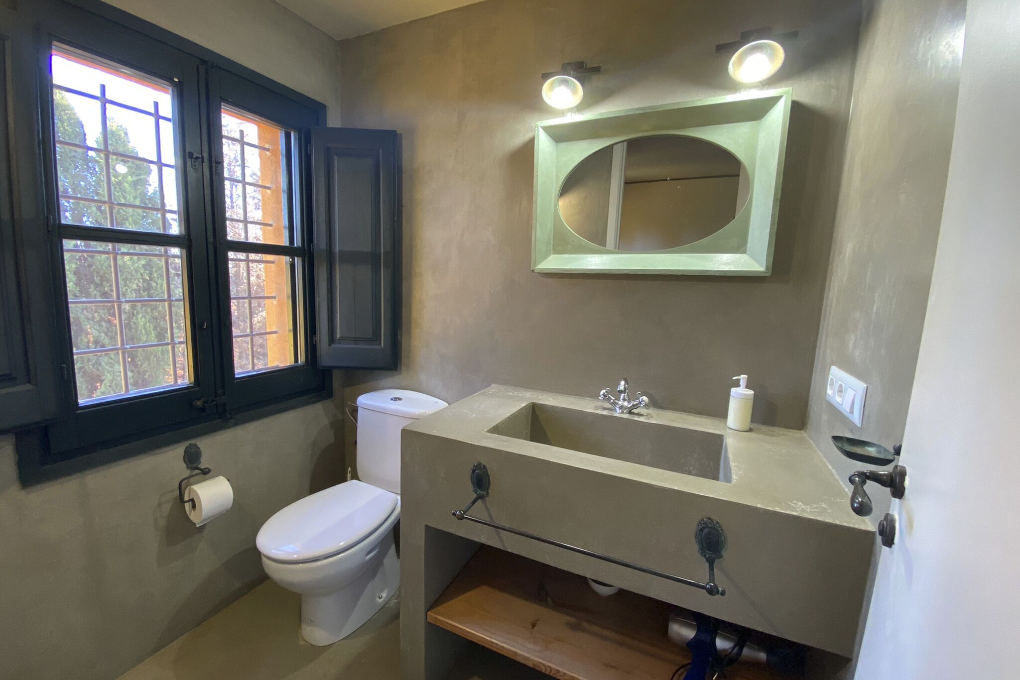 A bathroom with a toilet, sink, mirror, and window.
