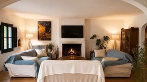 A cozy room with a fireplace, two sofas, a bed, and a TV. - Hostal Nou de Crespià (Crespià)