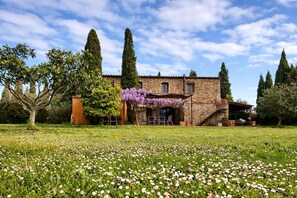 Un bâtiment en pierre avec un jardin devant, entouré d’arbres.