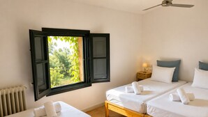 A room with two beds, a window with open shutters, a radiator, a ceiling fan, and a bedside table with a lamp. - Hostal Nou de Crespià (Crespià)