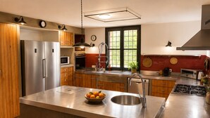A modern kitchen with stainless steel appliances, wooden cabinets, and a large island with a bowl of fruit. - Hostal Nou de Crespià (Crespià)