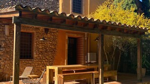 A stone building with a wooden pergola, outdoor seating, and a view of trees and a mountain. - Hostal Nou de Crespià (Crespià)