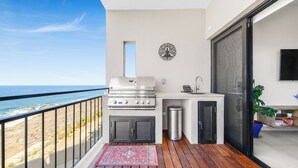 A balcony with a view of the beach, a grill, a sink, and a trash can. - 2BR/2BA Oceanfront Lux Surf Condo in Los Cerritos w/ Pool, Gym, Hot Tub, Sauna  (Los Cerritos)