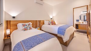 A hotel room with two beds, a wooden headboard, a bedside table with a lamp, a bathroom with a mirror, and a towel rack. - 2BR/2BA Oceanfront Lux Surf Condo in Los Cerritos w/ Pool, Gym, Hot Tub, Sauna  (Los Cerritos)
