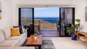 A living room with a sofa, coffee table, and a view of the ocean through a sliding glass door.