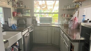 Cozinha compacta com armários brancos, micro-ondas e pia. Há uma janela que proporciona iluminação natural, e uma pequena área externa visível pela janela.