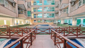 A multi-story hotel with a central courtyard featuring a swimming pool and wooden walkways. - Apartamento Praia do Cumbuco (Caucaia)