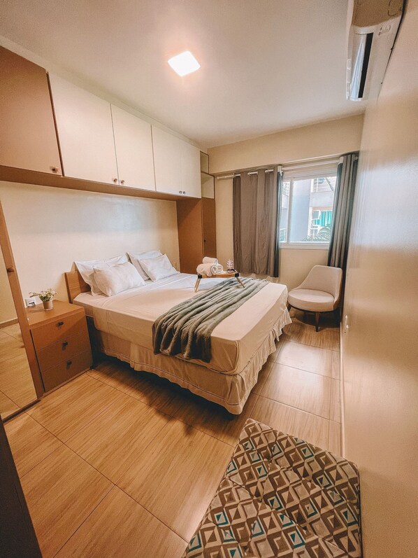 A hotel room with a bed, bedside table, chair, and a window with curtains.