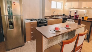 A modern kitchen with a central island, stainless steel appliances, and wooden cabinetry. - Apartamento Praia do Cumbuco (Caucaia)