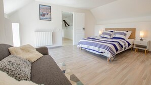 A bedroom with a bed, a nightstand, a lamp, a radiator, a sofa, and a poster on the wall. - L'Escale Champenoise (PLESSIS BARBUISE)