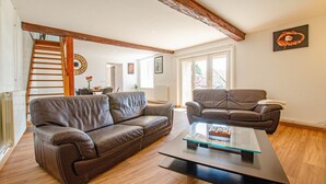 A spacious living room with a brown leather sofa, a glass coffee table, and a brown leather armchair. A wooden staircase leads to an upper level. - L'Escale Champenoise (PLESSIS BARBUISE)