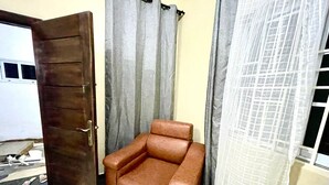 A room with a brown leather sofa, a wooden door, grey curtains, and a window with a grid pattern.