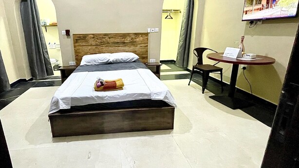 A hotel room with a bed, a small table with a chair, a TV, and a wall-mounted TV.