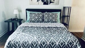 A bed with a geometric patterned bedspread and matching pillows, a bedside table with a lamp, and a wall art piece above the bed. - Harmonious Character & Comfort (Huntsville)