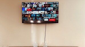 A flat-screen TV mounted on a wall displaying a Netflix interface with various shows and movies. Below the TV, there is a wooden cabinet with a label indicating it is a 42-inch electric fireplace. - Harmonious Character & Comfort (Huntsville)