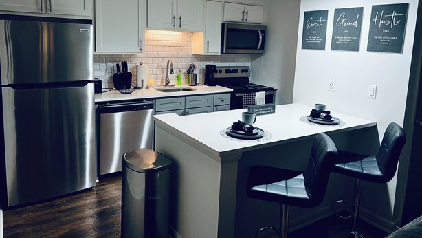 A modern kitchen with stainless steel appliances, a central island with bar stools, and motivational wall art. - Harmonious Character & Comfort (Huntsville)