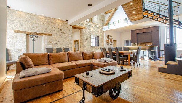 A spacious living area with a large L-shaped sofa, a coffee table, and a dining area with a high table and chairs.