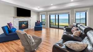 A spacious living room with a fireplace, a large sofa, a chair, and a view of the sea through large windows. - An amazing large group vacation home with elevator and breathtaking views. (Montross)