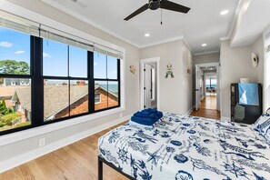 A bedroom with a large window, a ceiling fan, and a bed with a nautical-themed bedspread.
