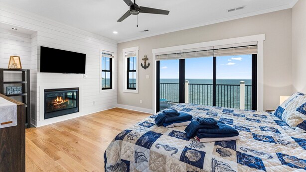 A bedroom with a large bed, a fireplace, a TV, and a balcony with a view of the ocean. - An amazing large group vacation home with elevator and breathtaking views. (Montross)