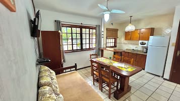 Cozinha compacta com área de refeições, móveis de madeira, ventilador de teto e geladeira.