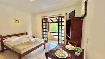 Habitación de hotel con una cama, una mesa de comedor con platos, una planta y un televisor montado en la pared.