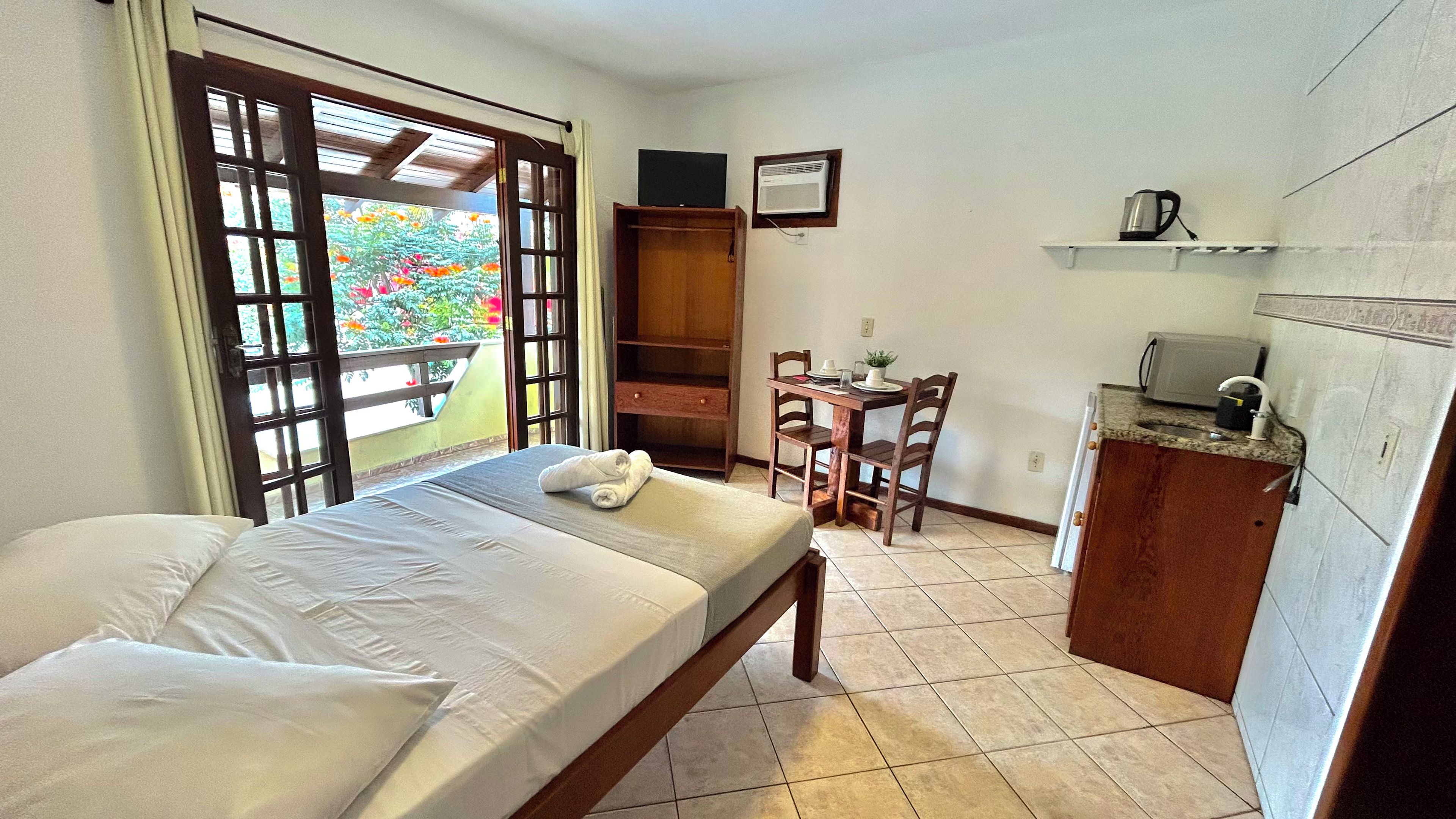 Quarto com cama, escrivaninha e pequeno espaço de cozinha.