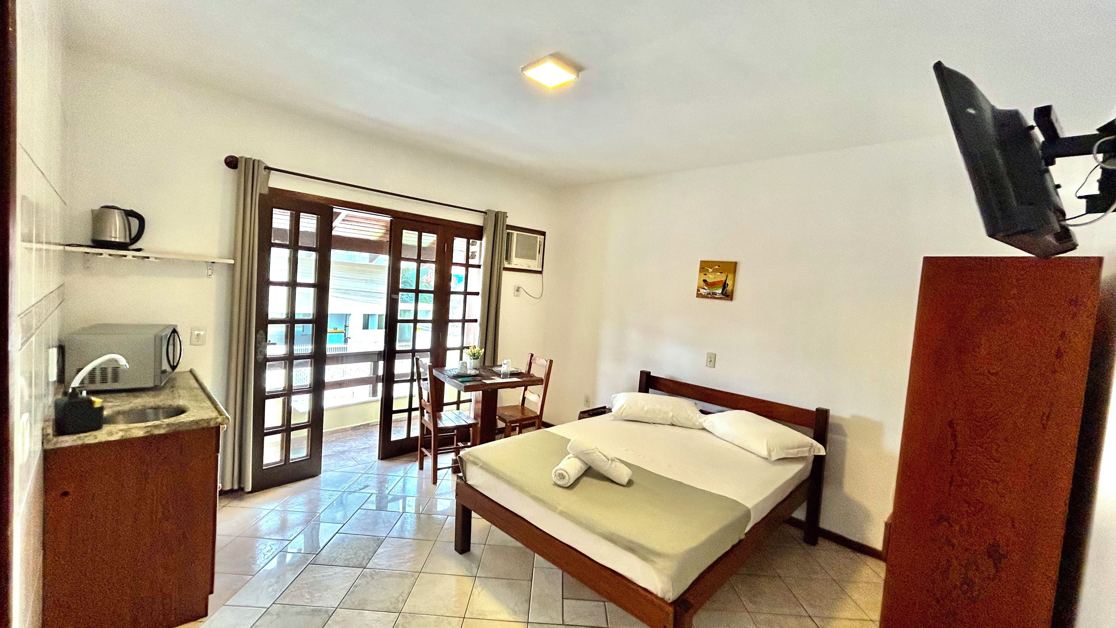 A hotel room with a bed, a desk, a chair, a television, and a view through a door.