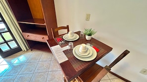 Una mesa de comedor con platos, vasos y cubiertos, una planta en maceta y una ventana con cortinas.