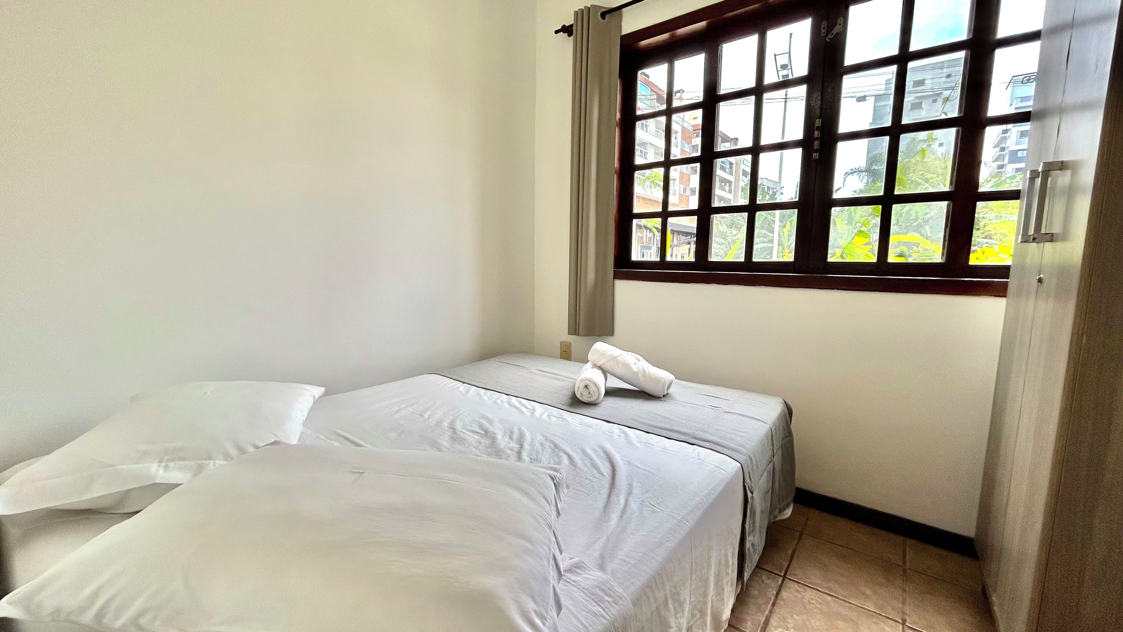 Una habitación pequeña y limpia con una cama, un ventanal con vistas a edificios y una puerta.