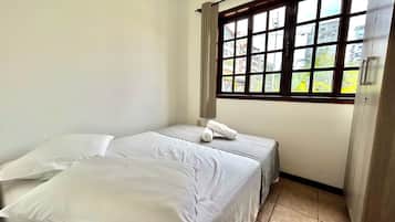 Una habitación pequeña y limpia con una cama, un ventanal con vistas a edificios y una puerta.
