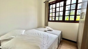 A small, clean room with a bed, a window with a view of buildings, and a door.