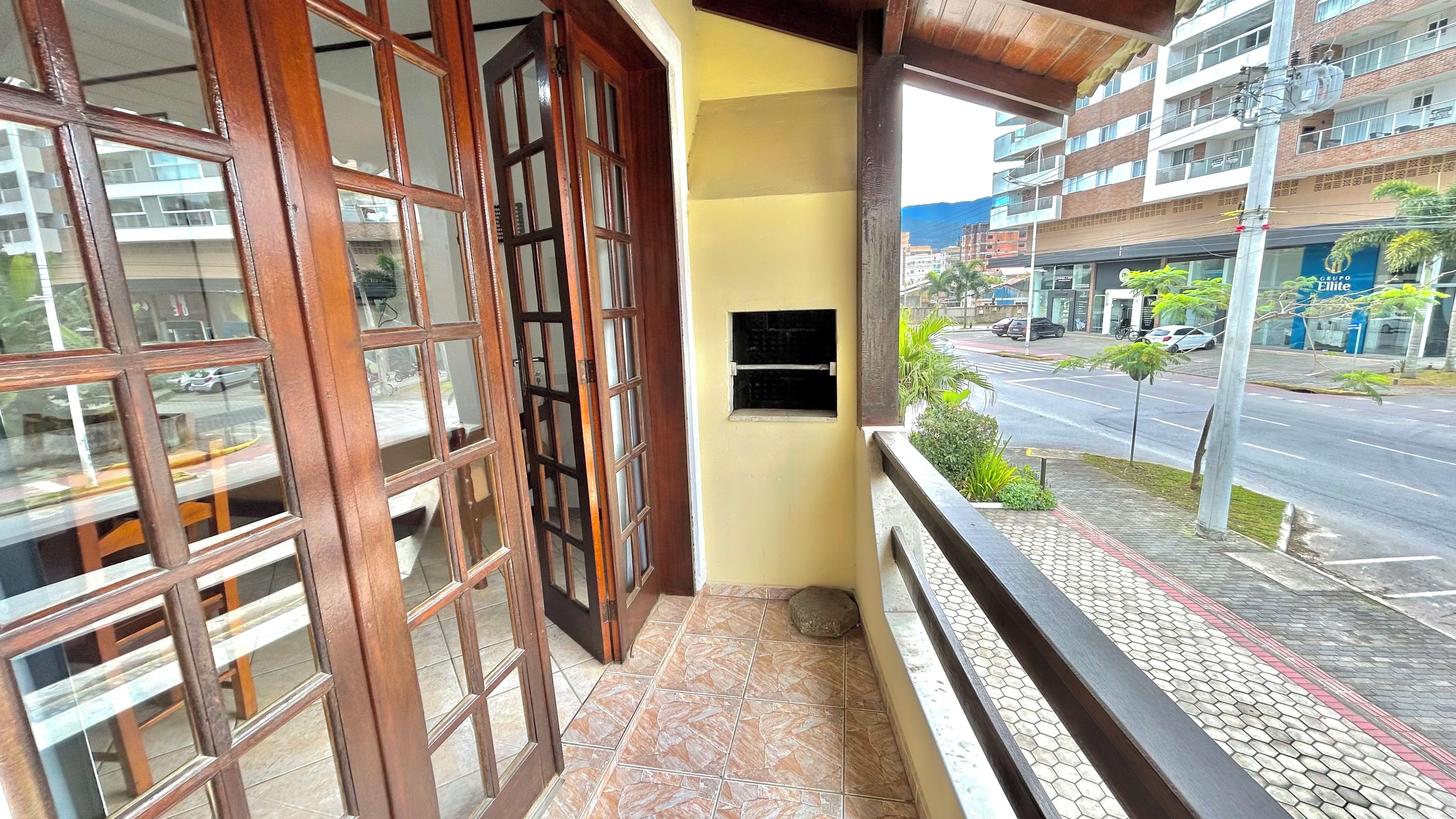 A balcony with a tiled floor, a wooden railing, and a view of a street with cars and buildings.