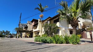 A residential street with houses, palm trees, and a paved sidewalk. - Pousada Jardim das Gales Bombinhas (Bombinhas)