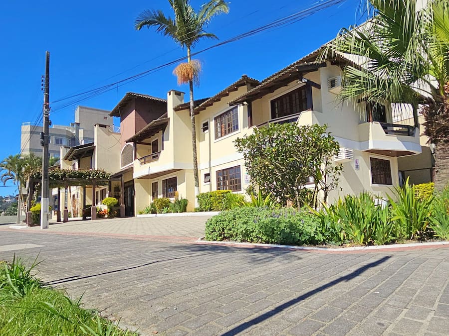 A residential building with multiple balconies, a paved driveway, and lush greenery including palm trees and shrubs.