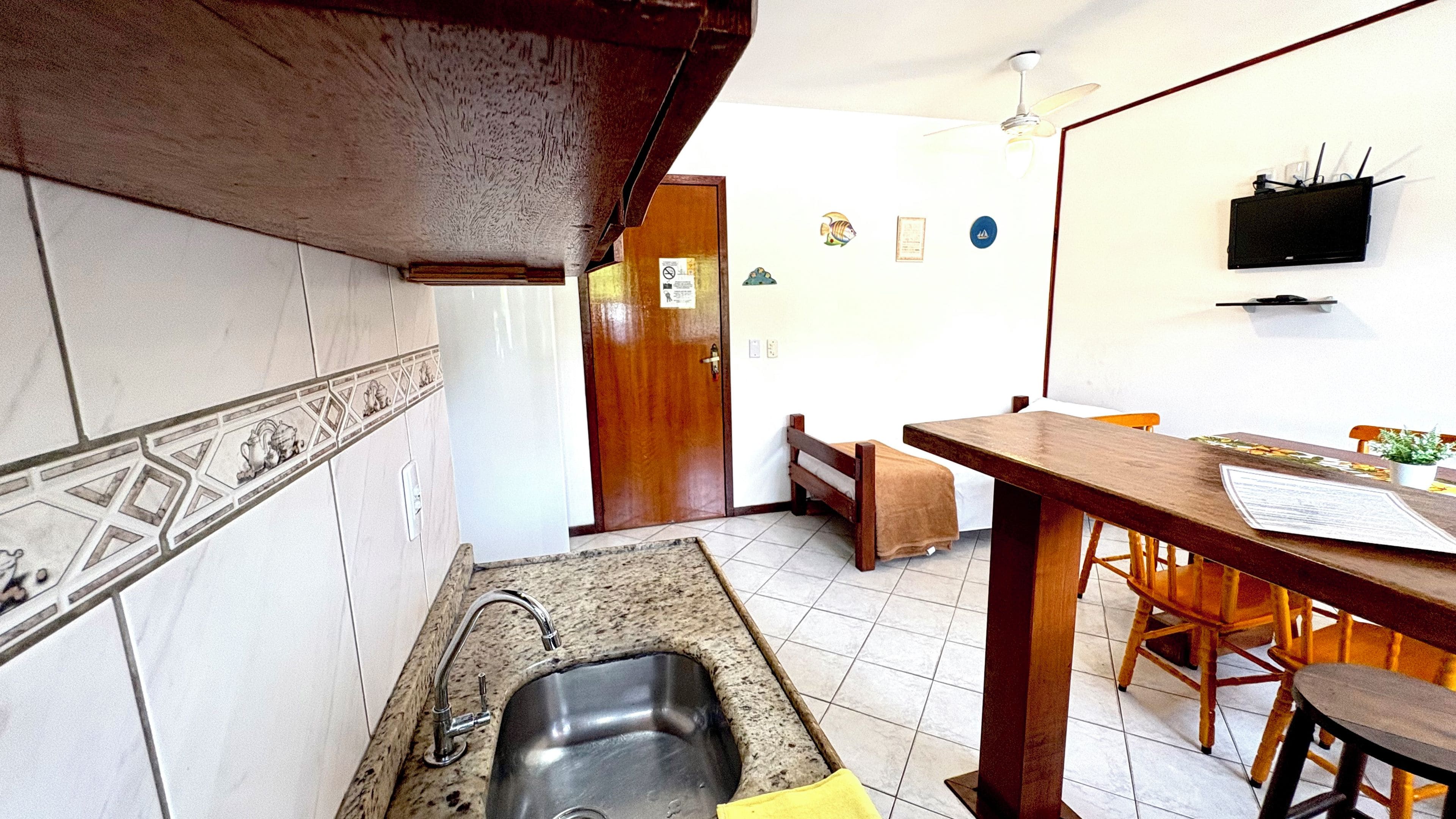 Una cocina con un lavamanos, armarios de madera, salpicadero de azulejos, zona de comedor con una mesa y sillas, y un ventilador de techo.