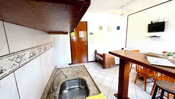 Una cocina con un lavamanos, armarios de madera, salpicadero de azulejos, zona de comedor con una mesa y sillas, y un ventilador de techo.