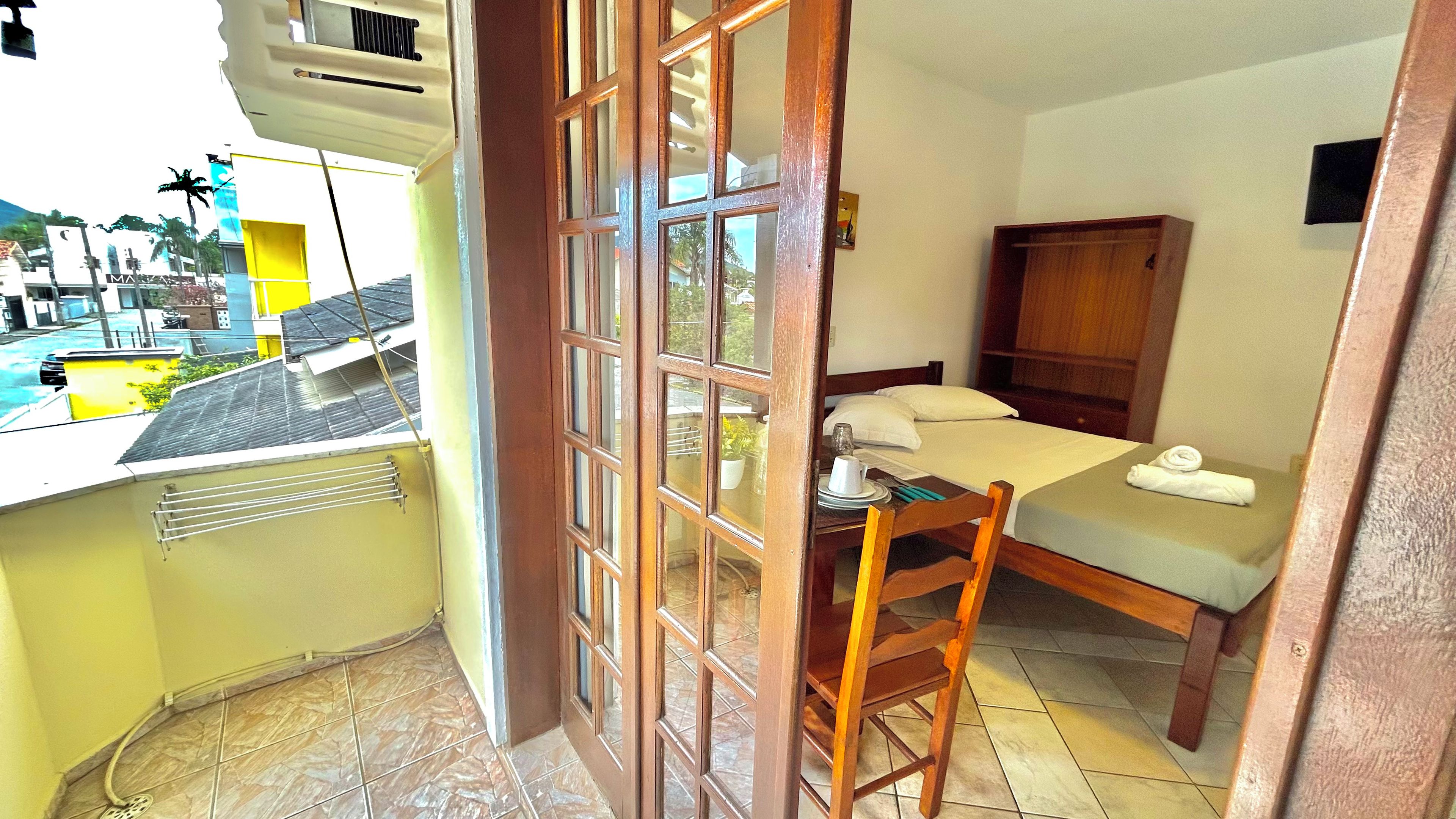 A compact room with a bed, a small table, and a chair. There is a window with a view of the outside.