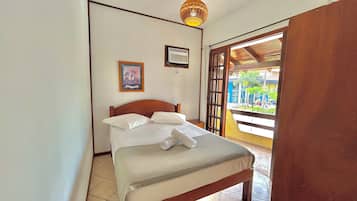 Un dormitorio con cama, aire acondicionado de pared, un cuadro enmarcado y vistas a través de una puerta abierta.
