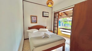 Un dormitorio con cama, aire acondicionado de pared, un cuadro enmarcado y vistas a través de una puerta abierta.