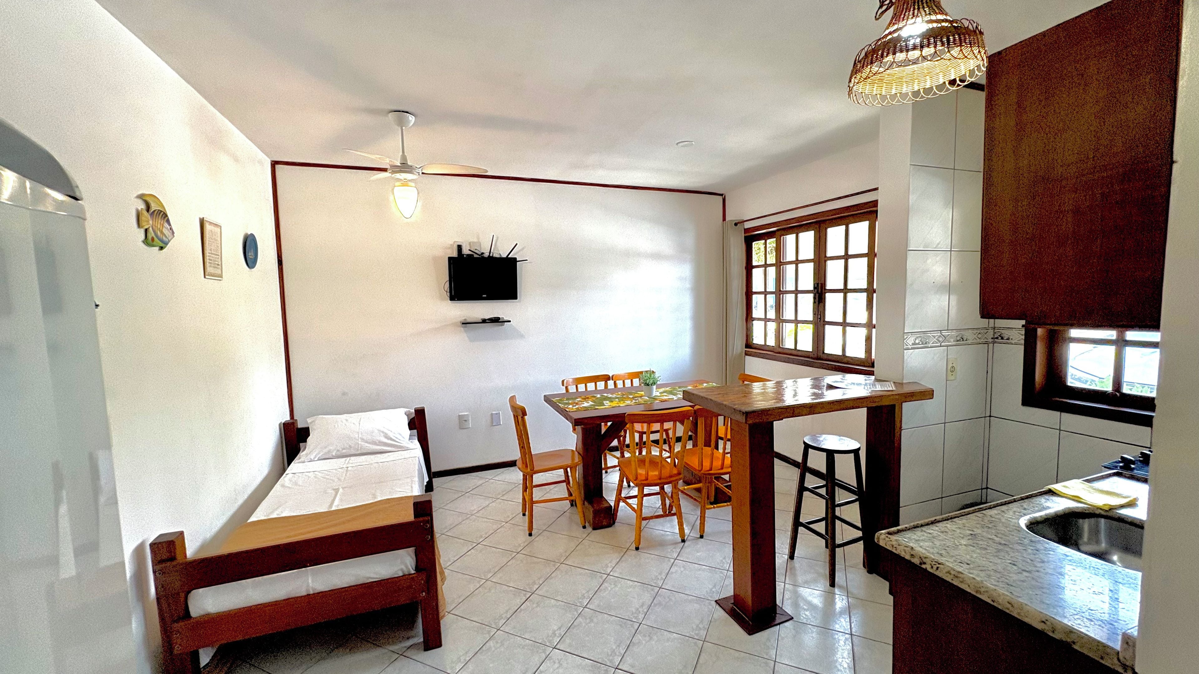 Cocina compacta con comedor, una cama individual y televisor montado en la pared.