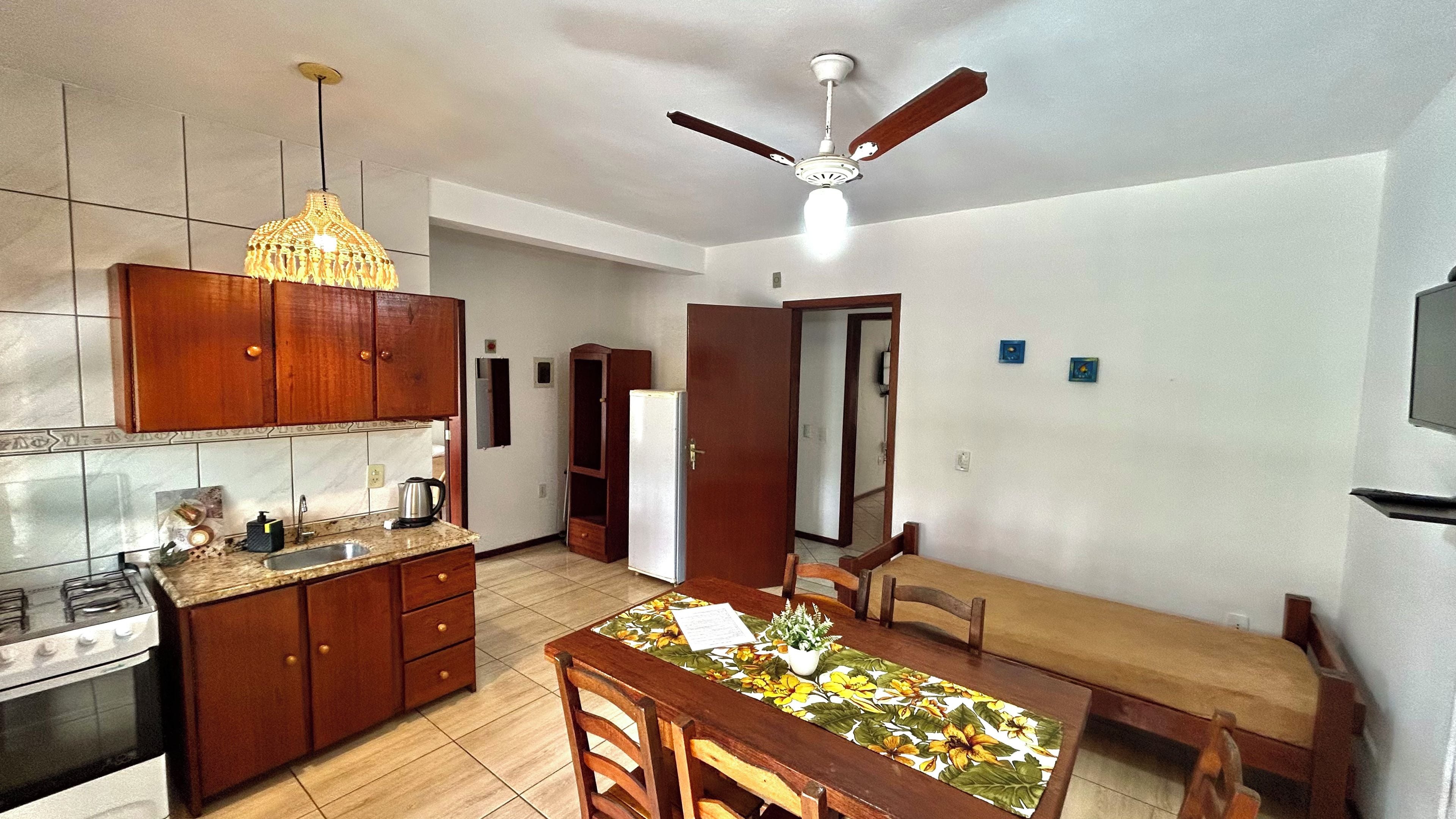 A compact kitchen with a gas stove, wooden cabinets, a dining table with chairs, and a ceiling fan.