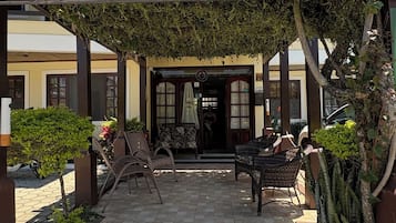 A covered outdoor seating area with a sign reading 'JARDIM DAS GALES' and a view of the building entrance.