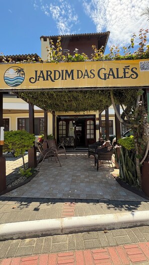 Een overdekt zitgedeelte met een bord waarop 'JARDIM DAS GALES' staat, met uitzicht op de ingang van het gebouw.