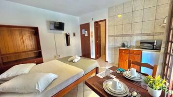 A hotel room with a bed, a TV mounted on the wall, a small kitchen area with a microwave, and a dining table set with plates and cutlery.