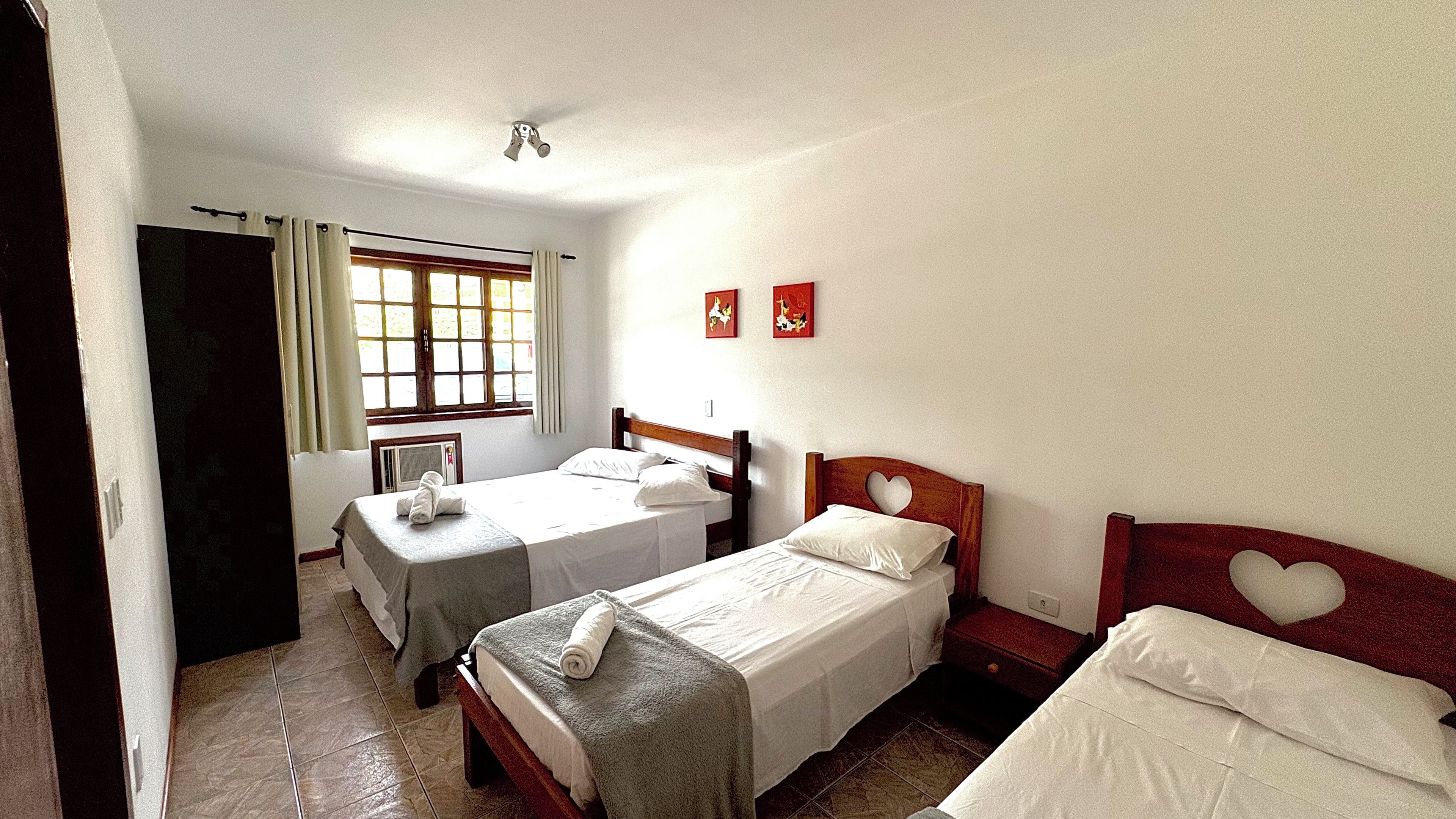 Una habitación de hotel con dos camas individuales, una ventana con cortinas, un calentador fijado a la pared y dos cuadros colgados.